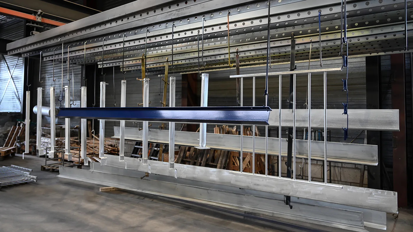 Blauw gepoedercoate ligger hangt naast kaal verzinkt werk aan de baan in de hal