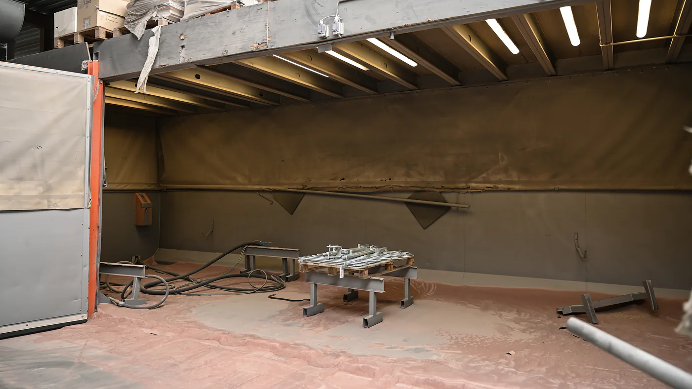 De straalcabine van Thermicoat, met straalmiddel op de vloer en het werk op de bok
